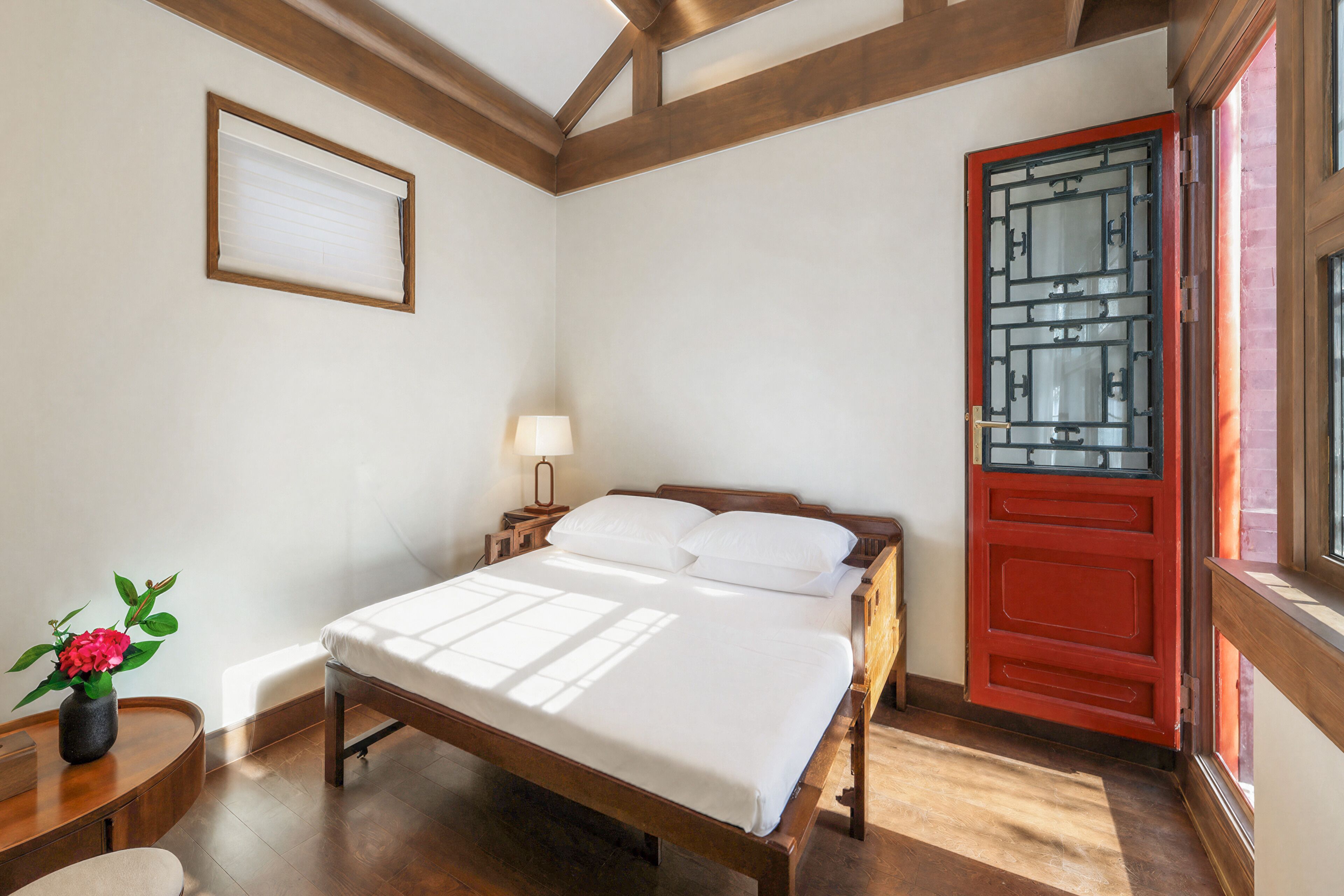 A bedroom with a wooden bed, a nightstand, a lamp, and a red door.
