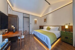 A hotel room with a bed, desk, chair, and a green dresser.