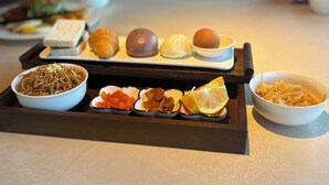 Uma bandeja com diversos alimentos, incluindo macarrão, bolinhos e um pão.