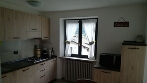Ett litet kök med träskåp, ett matbord med stolar, ett fönster med gardiner och en skylt med texten ”Kök”.