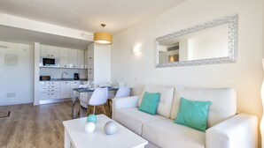 A modern living room with a white sofa, a coffee table, and a dining area with chairs and a table.