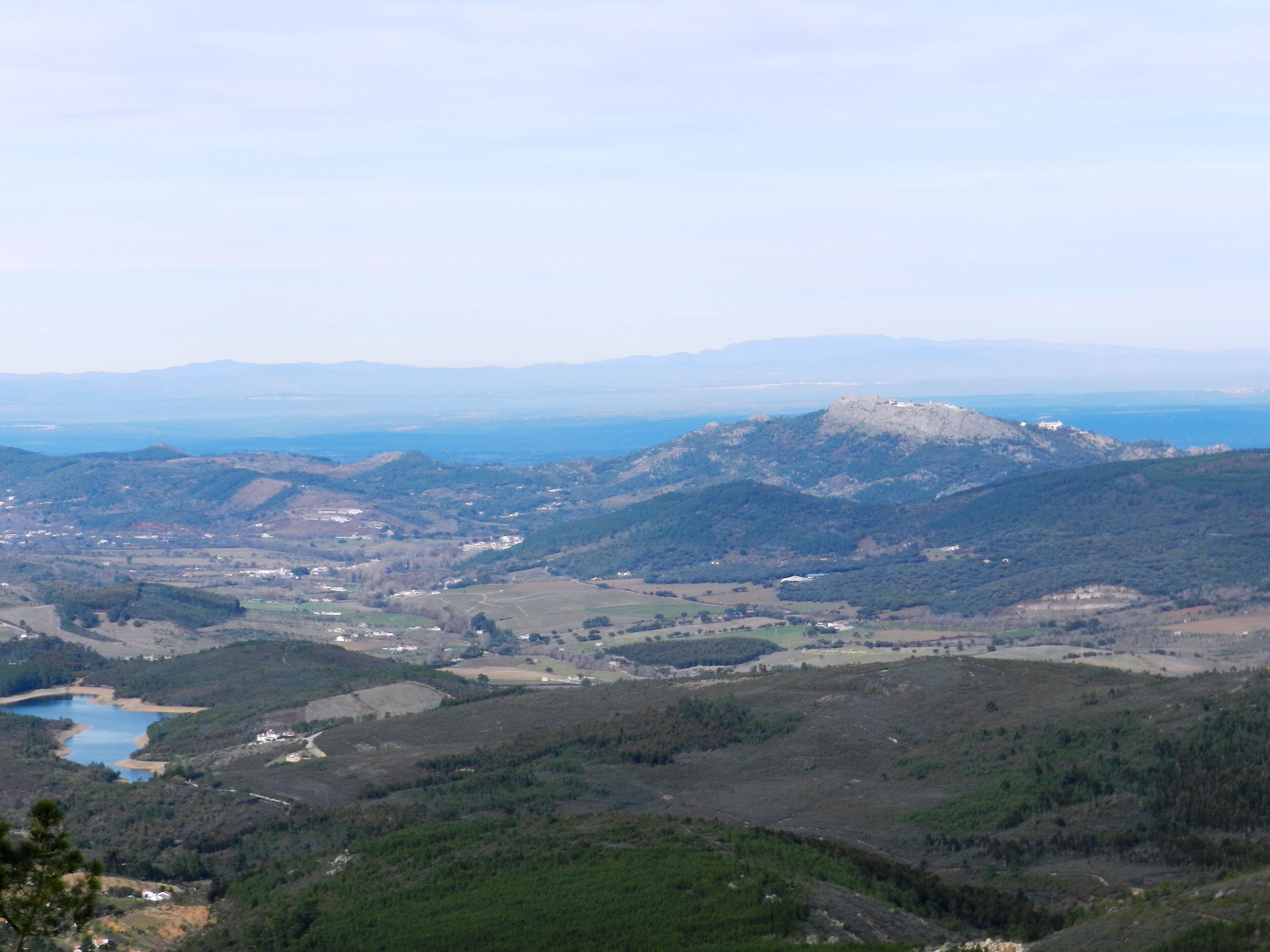Une vue panoramique d’un paysage montagneux, avec un sommet imposant, une vallée parsemée de bâtiments et une étendue d’eau.