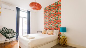 Une chambre à coucher avec un lit, un fauteuil vert, une table de chevet avec une lampe et un mur orné d’un motif de flamants roses.