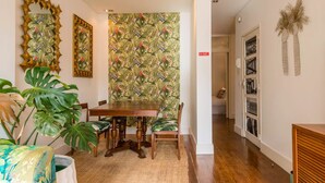 Un coin repas avec une table et des chaises en bois, entouré d’un papier peint aux motifs tropicaux et agrémenté d’une grande plante.