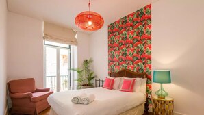 Une chambre à coucher avec un lit, une chaise, une lampe et un mur orné d’un motif de flamants roses.