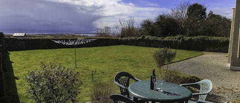 A patio with a table and chairs, a bottle of wine, and a view of the sea.