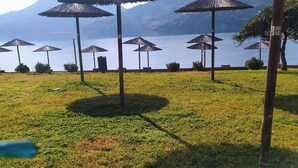 A grassy area with several thatched umbrellas and a view of a body of water with mountains in the background.