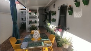 A small outdoor patio with a table and chairs, surrounded by potted plants and a white partition.