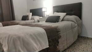 A hotel room with two beds, each with a headboard, a bedside table, and a lamp.