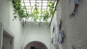A narrow hallway with a white door on the left, a white wall with blue striped decorations, and a hanging plant.