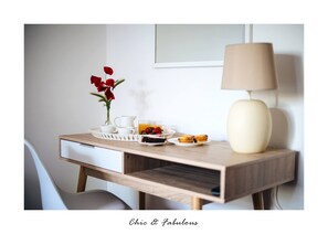 Uma mesa de pequeno-almoço bem arrumada com um vaso de flores vermelhas, uma lâmpada e um tabuleiro de comida.