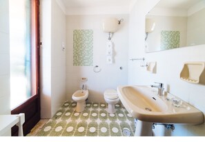 A bathroom with a bidet, toilet, sink, and a window with frosted glass.