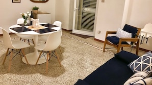 A living room with a round dining table, white chairs, a sofa with patterned cushions, a wooden chair, and a large mirror on the wall. - Sonetto holiday home in the center of Campomarino in Salento (Campomarino)
