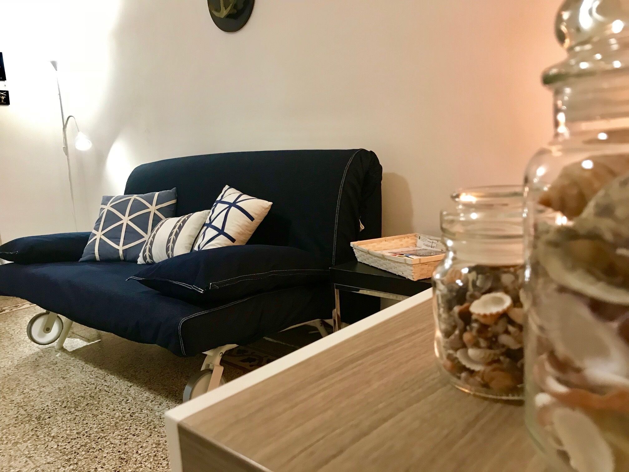 En stue med en mørkeblå sofa, et lille træsidebord og et glas med tørrede blomster.