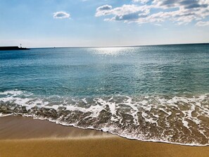Una playa con agua cristalina, olas y un barco a lo lejos.