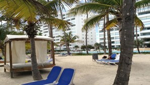 Uma área de praia com palmeiras, um bangalô de praia e cadeiras de descanso.