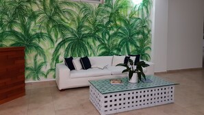 Uma sala de estar com um sofá branco, uma mesa de centro e uma parede com um mural de uma palmeira verde.