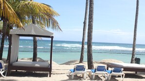 Uma praia com toldo, cadeiras de descanso e vista para o oceano.