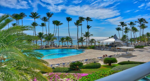 A resort with a swimming pool, beach area, and palm trees.