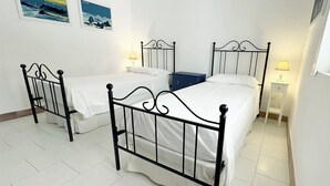 Une chambre avec trois lits simples, des murs blancs et un sol carrelé.