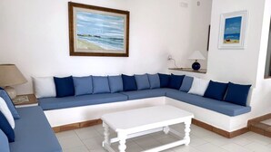 Un salon avec un canapé bleu, une table basse blanche et des tableaux représentant des plages, accrochés au mur.