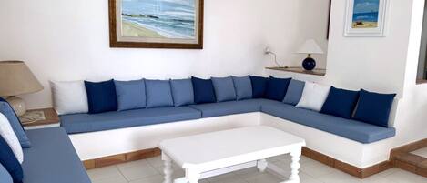 A living room with a blue sofa, white coffee table, and framed beach paintings on the wall.