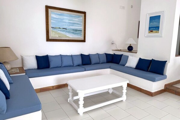 A living room with a blue sofa, white coffee table, and framed beach paintings on the wall.