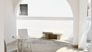 Un espace extérieur aménagé avec des sièges, offrant une vue sur la mer, comprenant une table ronde et deux chaises, un banc en pierre et une arche blanche.