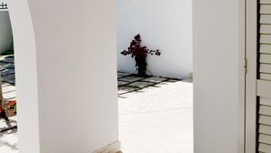 Un couloir intérieur aux murs blancs, agrémenté d’arches, doté d’un sol carrelé et d’une porte avec une fenêtre.