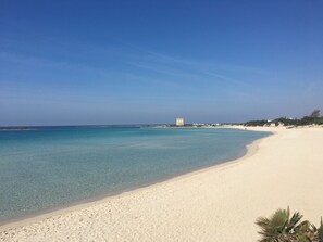A beach with clear turquoise water, white sand, and a tower structure in the distance.
