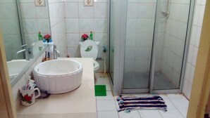 Um banheiro com pia branca, dois vasos sanitários, chuveiro e um tapete verde no chão.