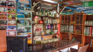 Um pequeno bar com tema de ilha, com um balcão de madeira, cadeiras de vime e diversas estantes cheias de livros e garrafas.