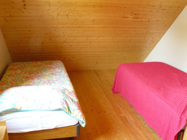 A small, single-bed room with a wooden ceiling and floor, a floral bedspread, and a pink blanket. - Group lodging in Mont St Michel Bay (Saint-Martin-des-Champs)