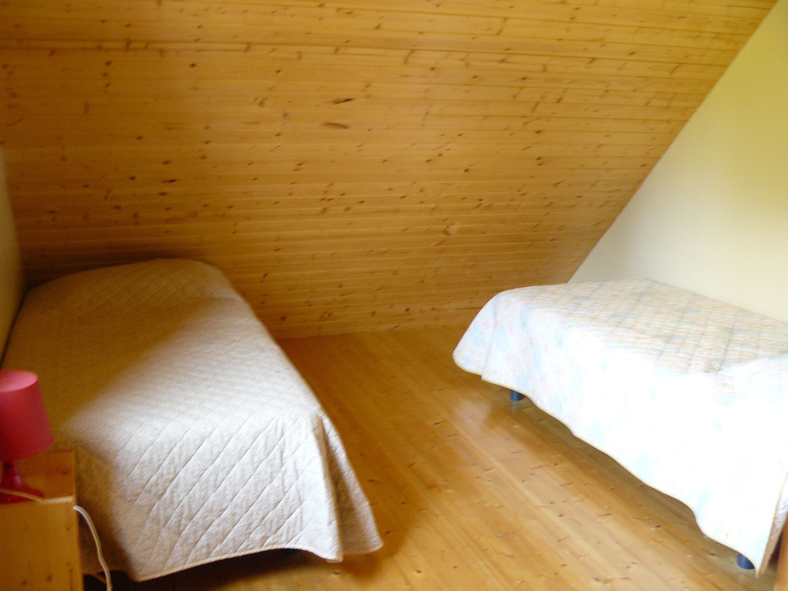 Un alojamiento pequeño y de una sola habitación con dos camas, paredes de madera y techo inclinado.