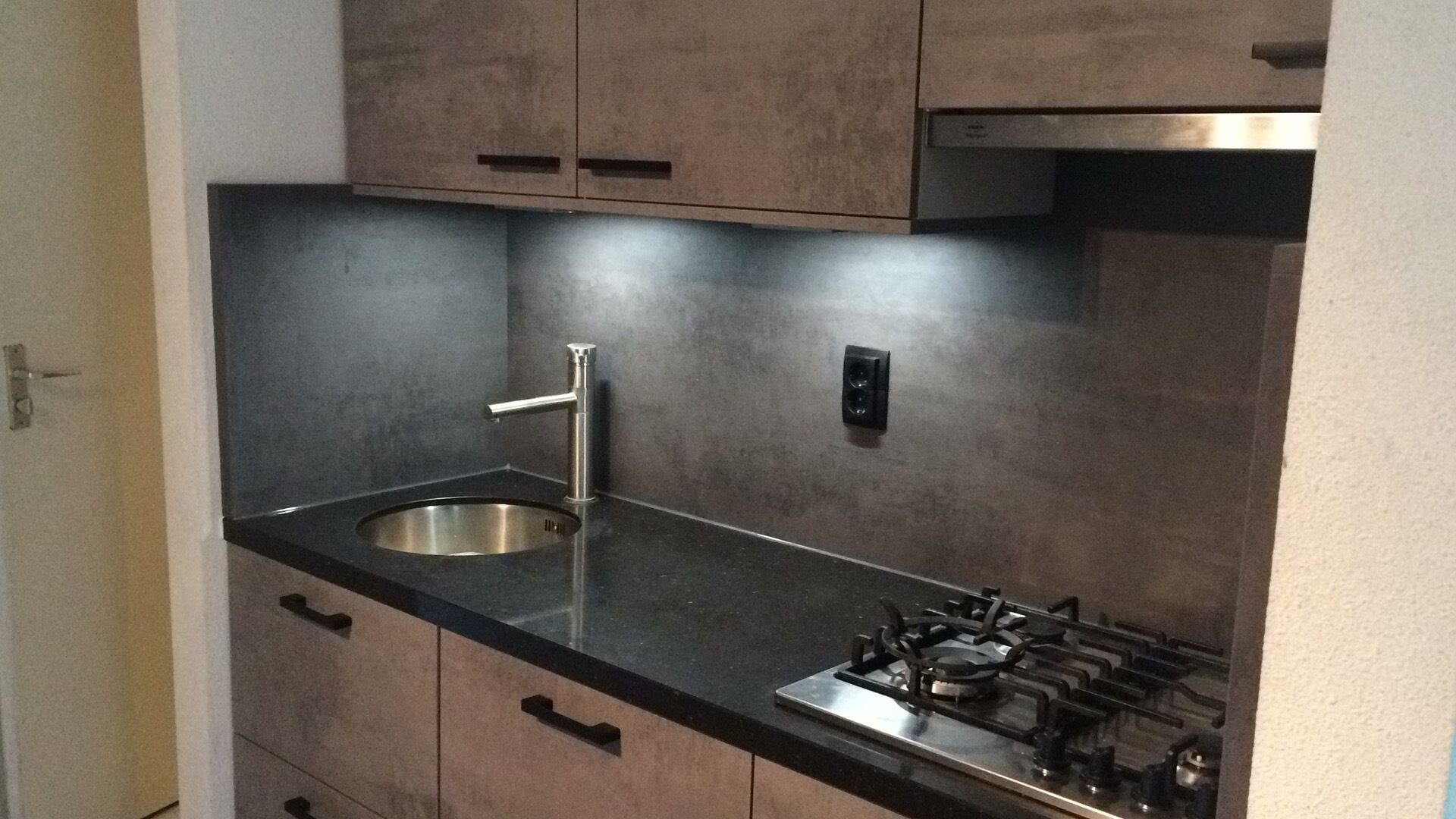 Een moderne keuken met een roestvrijstalen spoelbak, een gasfornuis en houten kastjes.