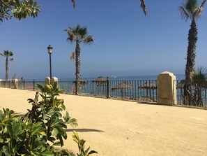 Eine Küstenpromenade mit Palmen, einem Sandweg und freiem Blick auf das Meer.