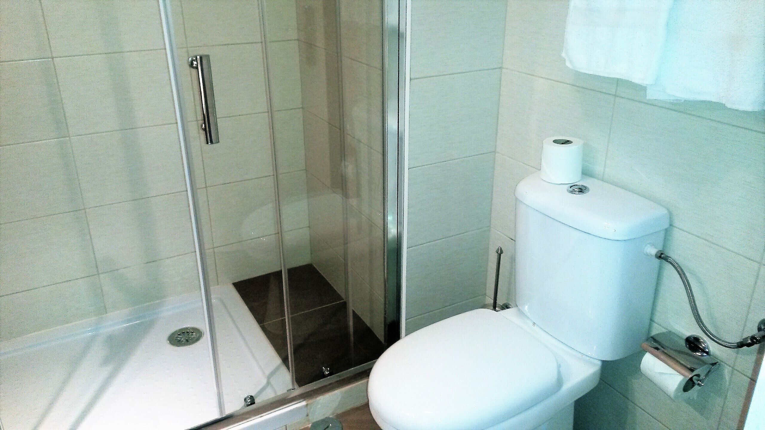 Un baño con cabina de ducha de vidrio, inodoro y una toalla colgada en la pared.
