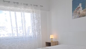 A neatly made bed with folded towels, a bedside lamp, and a window with sheer curtains. - Torre 6- Family, Wi-fi, Central and 80mt Beach (Quarteira)