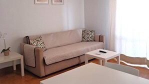 A modern living room with a beige sofa, a white coffee table, and a white dining table. There are two framed pictures on the wall, a potted plant, and a ceiling light. - Torre 6- Family, Wi-fi, Central and 80mt Beach (Quarteira)