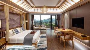 Una habitación de hotel moderna con una cama grande, zona de comedor, televisor y vistas a la ciudad.