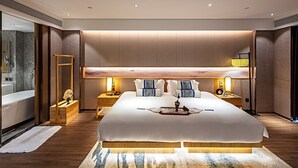 Una habitación de hotel moderna con una cama grande, mesitas de noche, un banco de madera y un ventanal amplio.