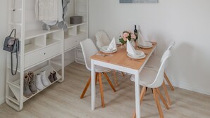 A dining area with a white table set for four, surrounded by white chairs. A white shelving unit with shoes and a handbag is to the left. - Ansbachs City Apartment (Ansbach)