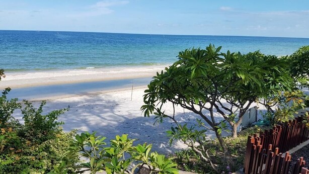 A beach view with a staircase leading down to the sand, surrounded by greenery and a wooden fence. - Baan San Dao Hua Hin (Hua Hin)