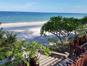 A beach view with a staircase leading down to the sand, surrounded by greenery and a wooden fence. - Baan San Dao Hua Hin (Hua Hin)
