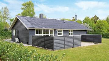 Une maison moderne à deux étages, avec une façade de couleur gris foncé, un toit en pente et une cour arrière clôturée.