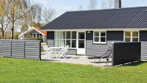 Ett modernt hus med ett mörkt tak, stora fönster och en uteplats med utemöbler.