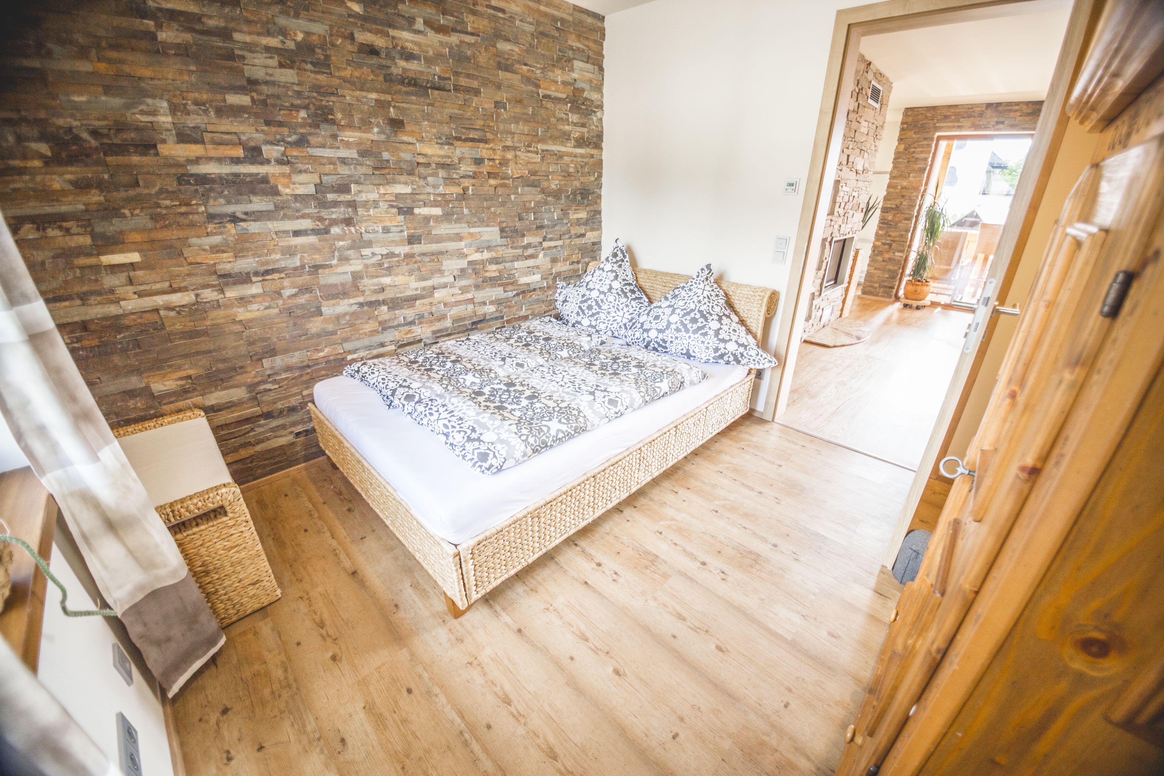 Une chambre avec un plancher en bois, un lit recouvert d’une literie à motifs, un mur en pierre et une porte en bois.