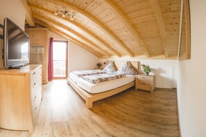 Un dormitorio con techo de madera, una cama con ropa de cama estampada, un televisor sobre un tocador de madera y una mesita de noche con una planta.