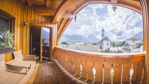 A wooden balcony with wicker furniture, a view of a church, and mountains in the background.