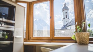 A kitchen with a large window overlooking a mountain and a church steeple.